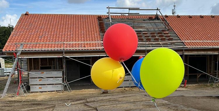 Bygning med byggematerialer og stillads foran og en række farverige balloner i en snor i forgrunden. 
