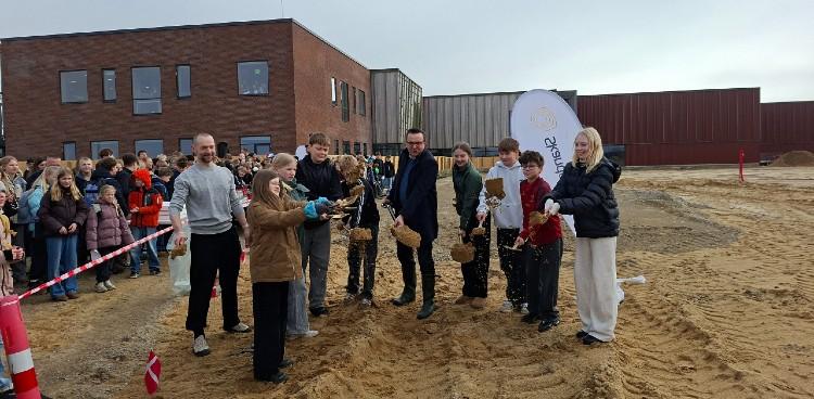 Billedet viser borgmester Frands Fischer og otte elever fra Sommerbæk Skole, der sammen tager første spadestik til anden etape af skolebyggeriet. Foto: Skanderborg Kommune