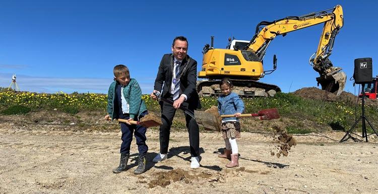 Frands Fischer med borgmesterkæden om halsen holder en spade med jord på. Ved siden af står to børn med jord på deres børnespader. I baggrunden er der en gravemaskine.