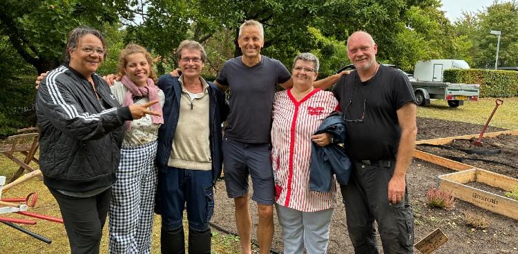 Foto af seks mennesker på række med armene om hinanden. Smiler og en kaster håndtegn. De står foran de havelodder, som er blevet anlagt gennem projektet. Foto: Skanderborg Kommune 