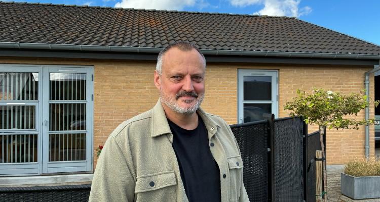 Billede af Karsten Marott Jørgensen foran sin gule murstensvilla i Herskind. I baggrunden ses det tag, hvorpå der skal installeres solceller.