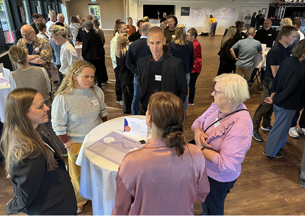 Mange mennesker i samtale ved en række høje cafeborde.