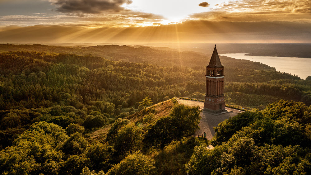 Dronefoto af Himmelbjerget i varmt sollys, der bryder gennem skyerne. 